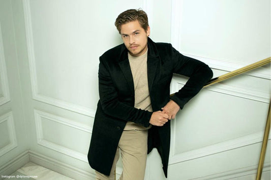 American actor Dylan Sprouse is wearing the SENTALER Technical Suri Alpaca Notched Lapel Overcoat in Black posing against a staircase.