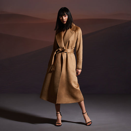 Image features the Fashion logo and an image of a female model wearing the Sentaler Suri Alpaca Long Notched Collar Raglan Sleeve Wrap Coat featured in Suri Alpaca and available in Dark Camel. Seen from front belted.