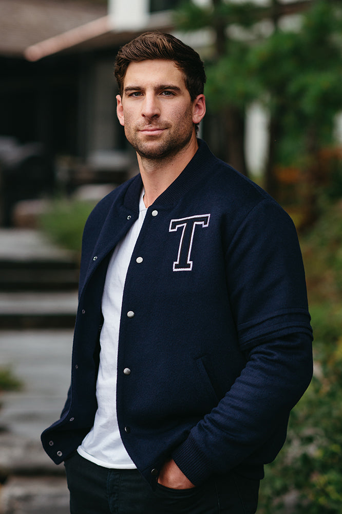 Image features the WWD logo and an image of Image features the Fashion logo and an image of Toronto Maple Leafs Captain, John Tavares wearing the SENTALER x John Tavares Varsity Jacket in Technical Baby Alpaca in Deep Navy. 