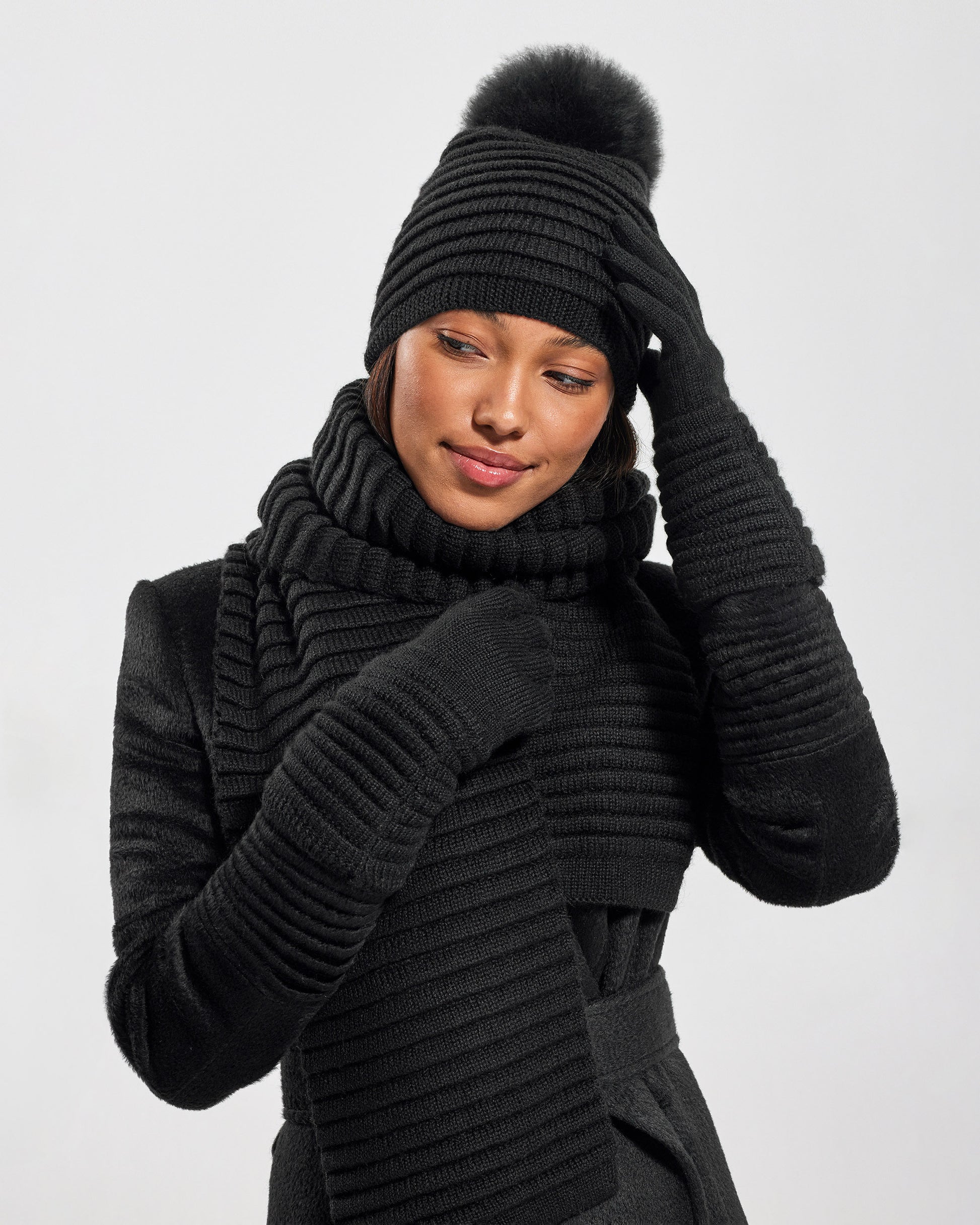 Front view of model wearing Sentaler's signature black ribbed hat, scarf, and gloves, paired with a matching black coat.