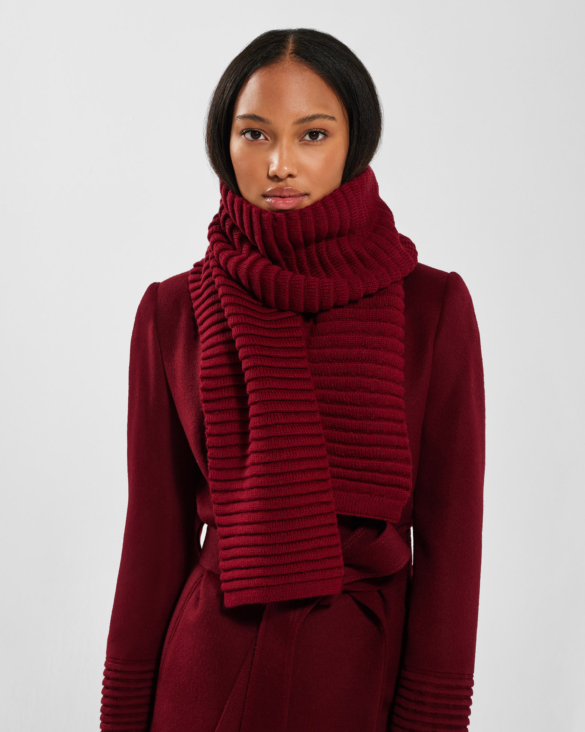 Front view of model wearing Sentaler's signature garnet red ribbed scarf, paired with a matching garnet red coat.