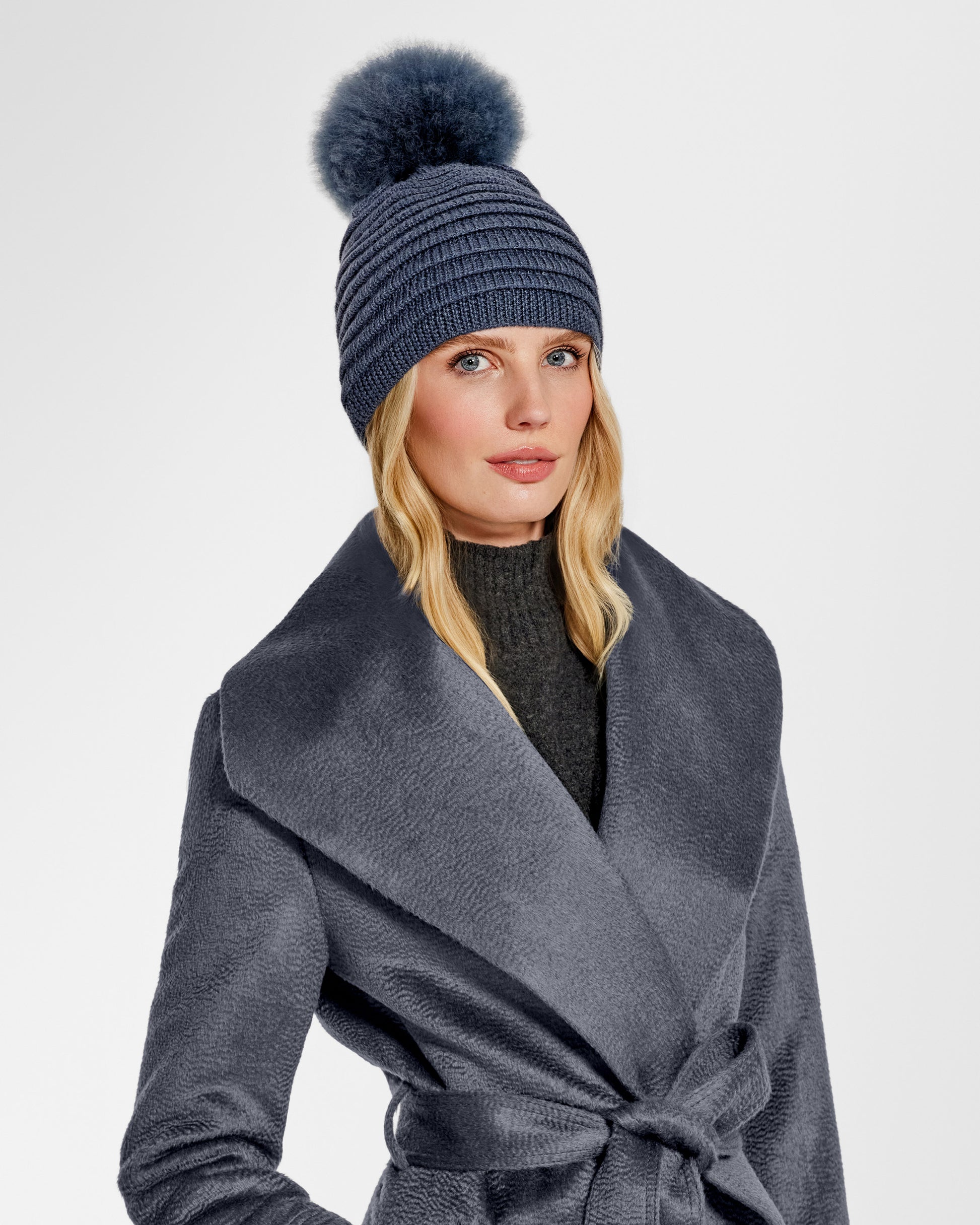 Front view of model wearing Sentaler's signature graphite ribbed hat with oversized fur pompon paired with a matching graphite coat.