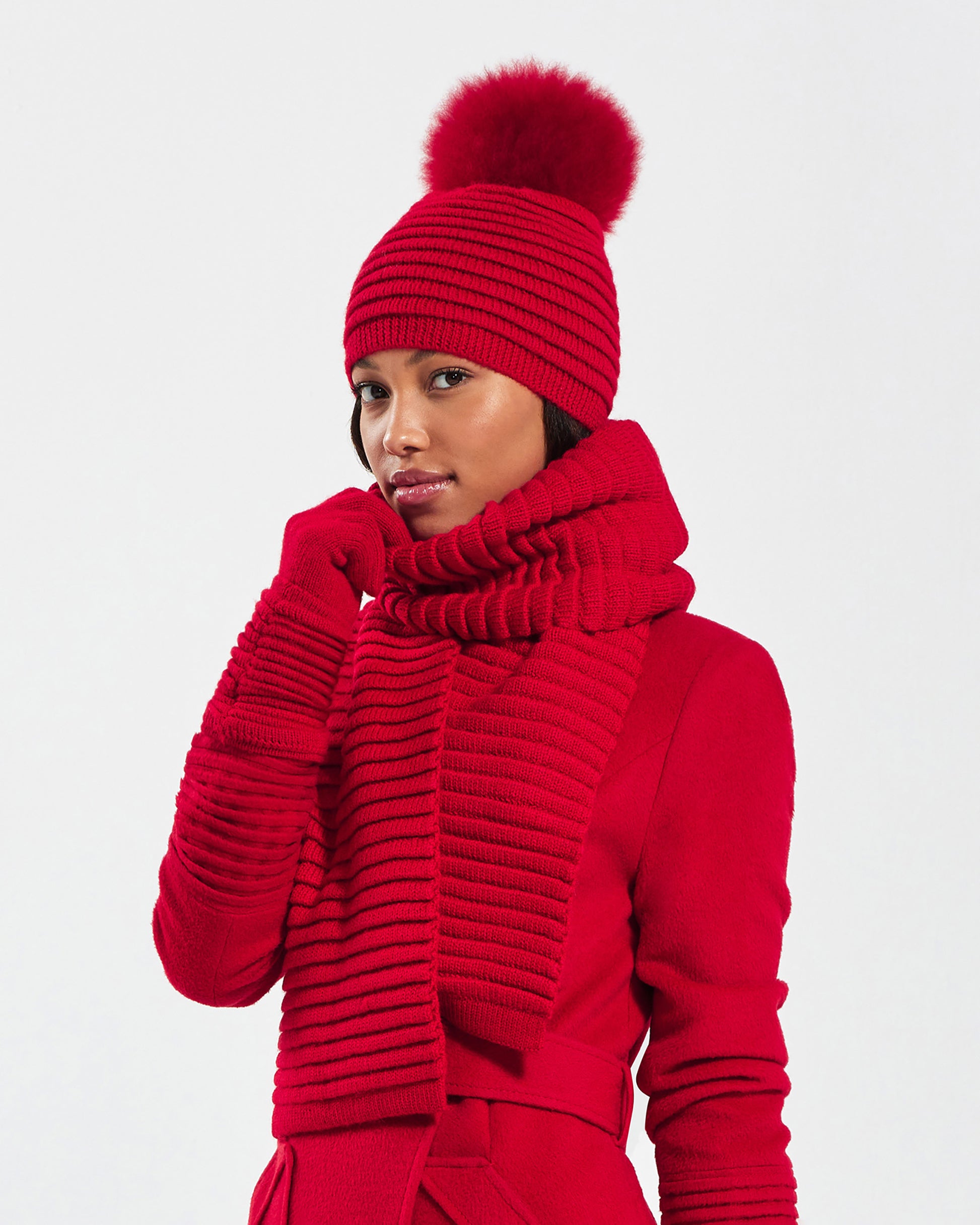 Side view of model wearing Sentaler's signature red ribbed hat, scarf, and gloves, paired with a matching scarlet red coat.