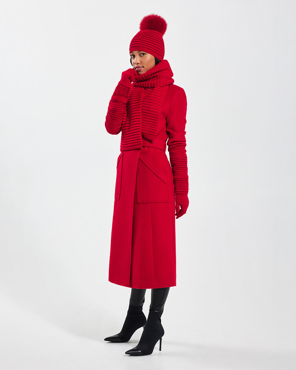 Side view of model wearing Sentaler's signature red ribbed hat, scarf, and gloves, paired with a matching scarlet red coat.