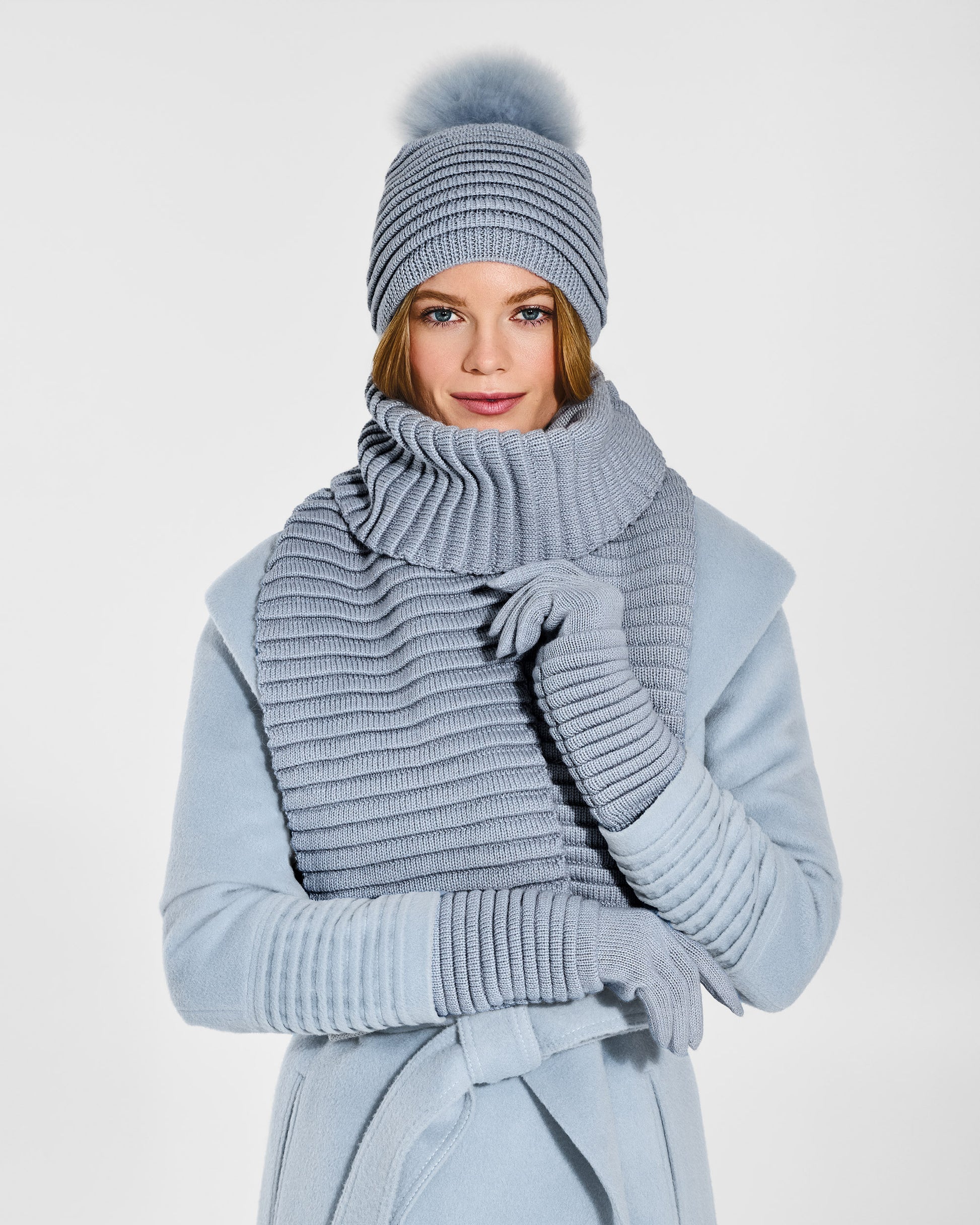Front view of model wearing Sentaler's signature glacial blue ribbed hat, scarf, and gloves, paired with a matching glacial blue coat.