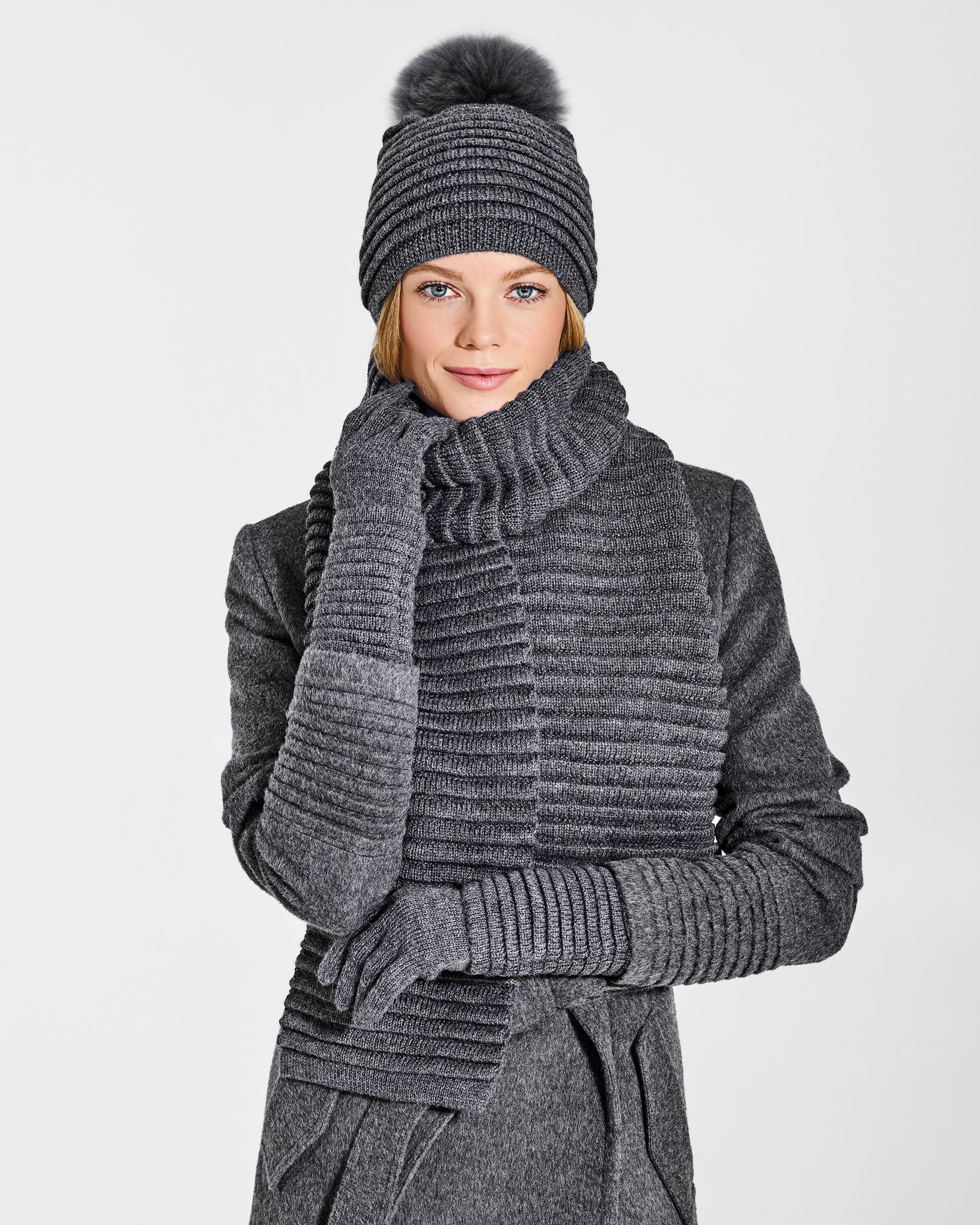 Front close up view of model wearing Sentaler's signature grey mélange ribbed hat, scarf, and gloves, paired with a matching grey mélange coat.