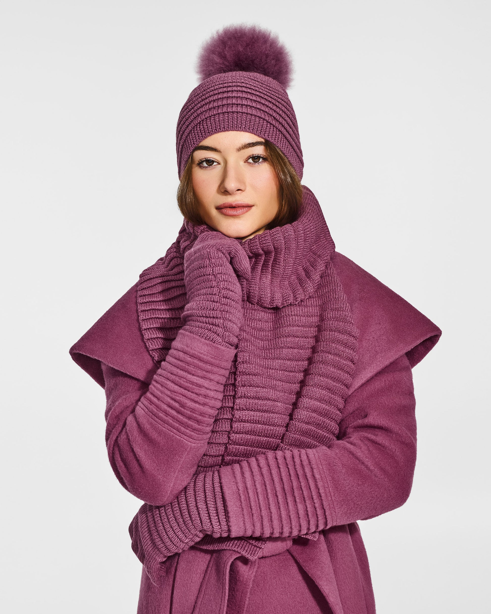 Front view of model wearing Sentaler's adult mauve pink ribbed hat with fur pompon, made of baby alpaca yarn, paired with a mauve pink coat.