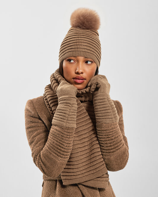 Sentaler Adult Ribbed Dark Camel Gloves, Adult Ribbed Dark Camel Hat With Fur Pompon, and Adult Ribbed Dark Camel Scarf in Baby Alpaca yarn. Seen from front close up on female model.