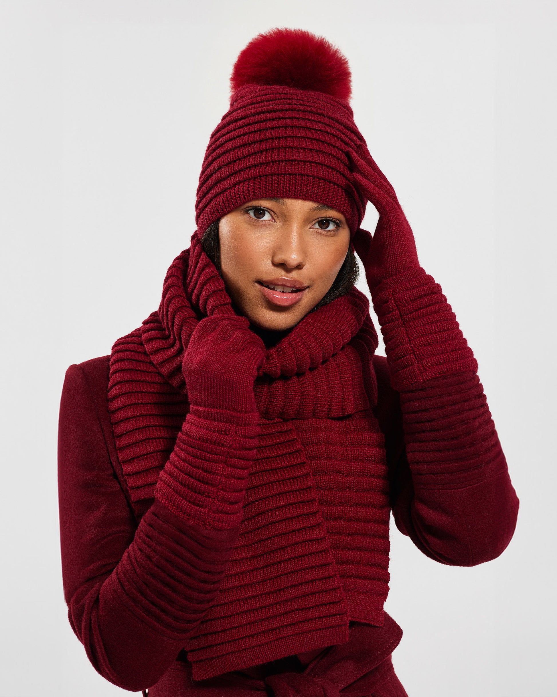 Front view of model wearing Sentaler's adult garnet red ribbed gloves, made of baby alpaca yarn, paired with a garnet red coat.