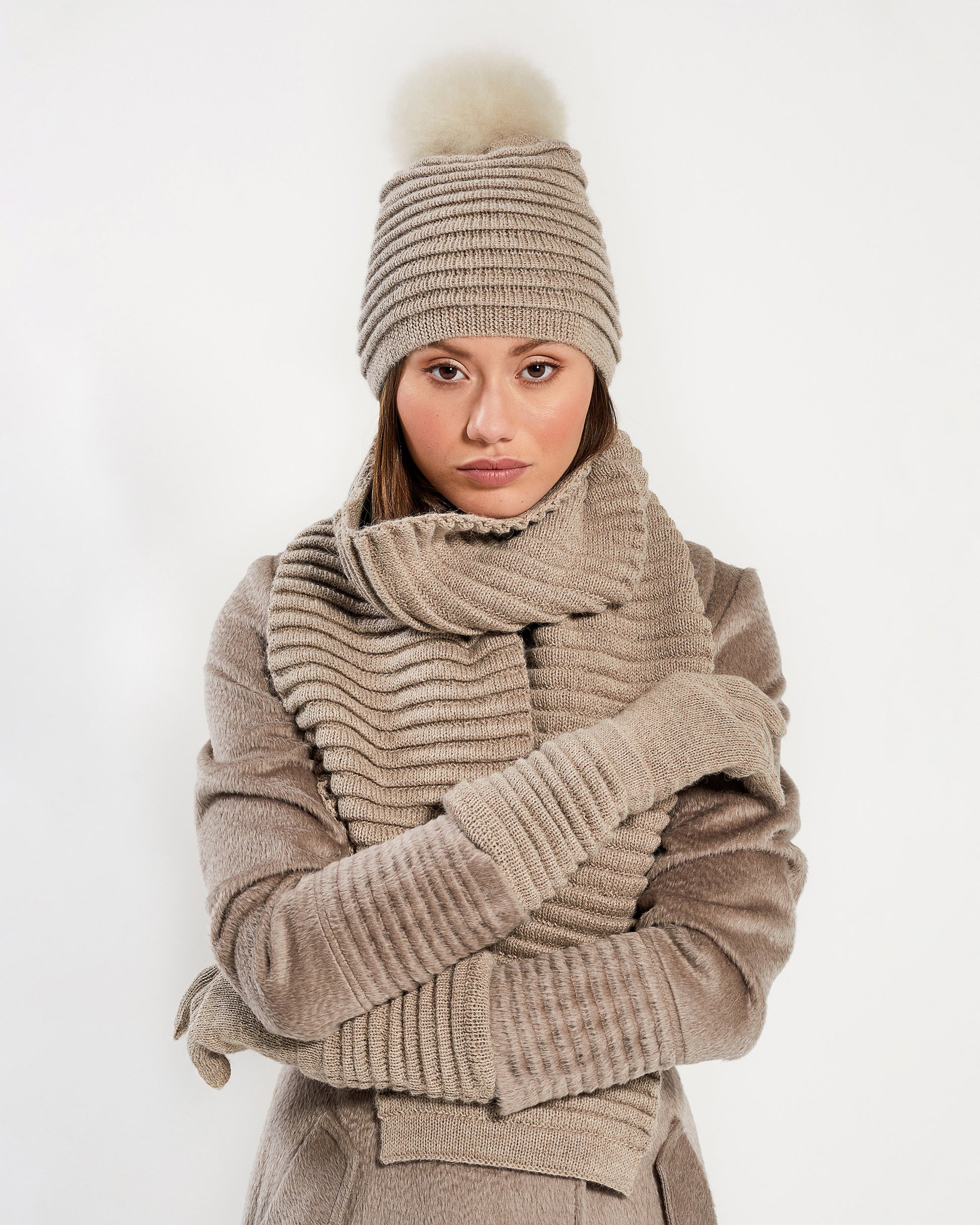 Front view of model wearing Sentaler's adult light taupe ribbed gloves, made of baby alpaca yarn, paired with a light taupe coat.