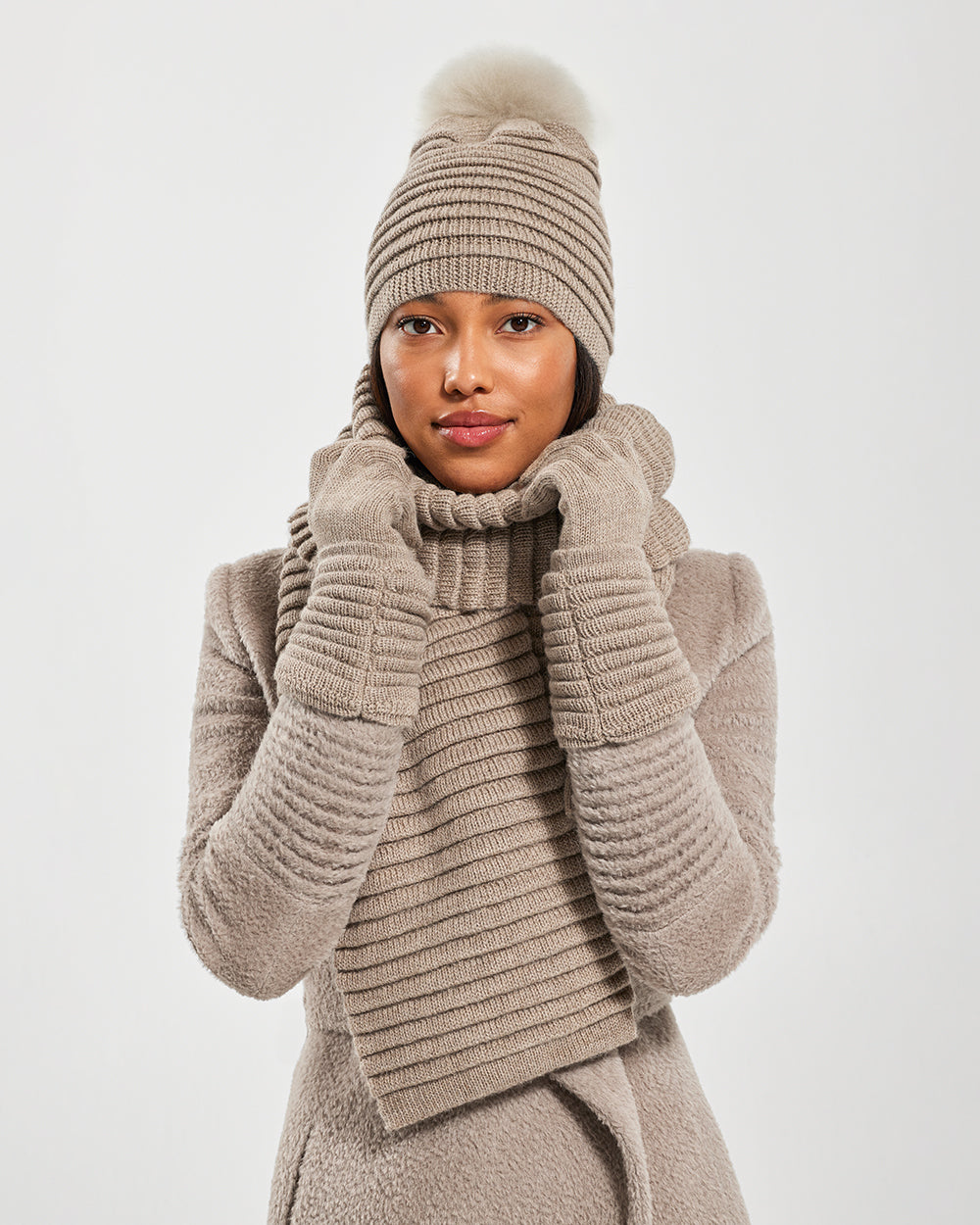 Sentaler Adult Ribbed Light Taupe Gloves, Adult Ribbed Light Taupe Hat With Fur Pompon, and Adult Ribbed Light Taupe Scarf in Baby Alpaca yarn. Seen from front close up on female model.