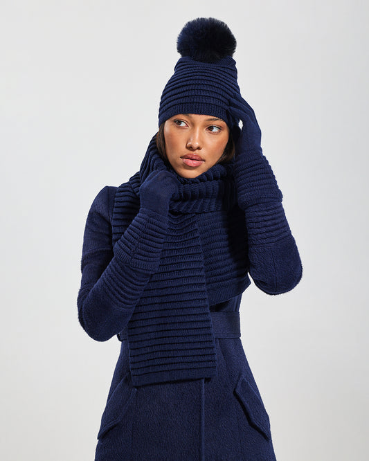 Sentaler Adult Ribbed Navy Gloves, Adult Ribbed Navy Hat With Fur Pompon, and Adult Ribbed Navy Scarf in Baby Alpaca yarn. Seen from front close up on female model.