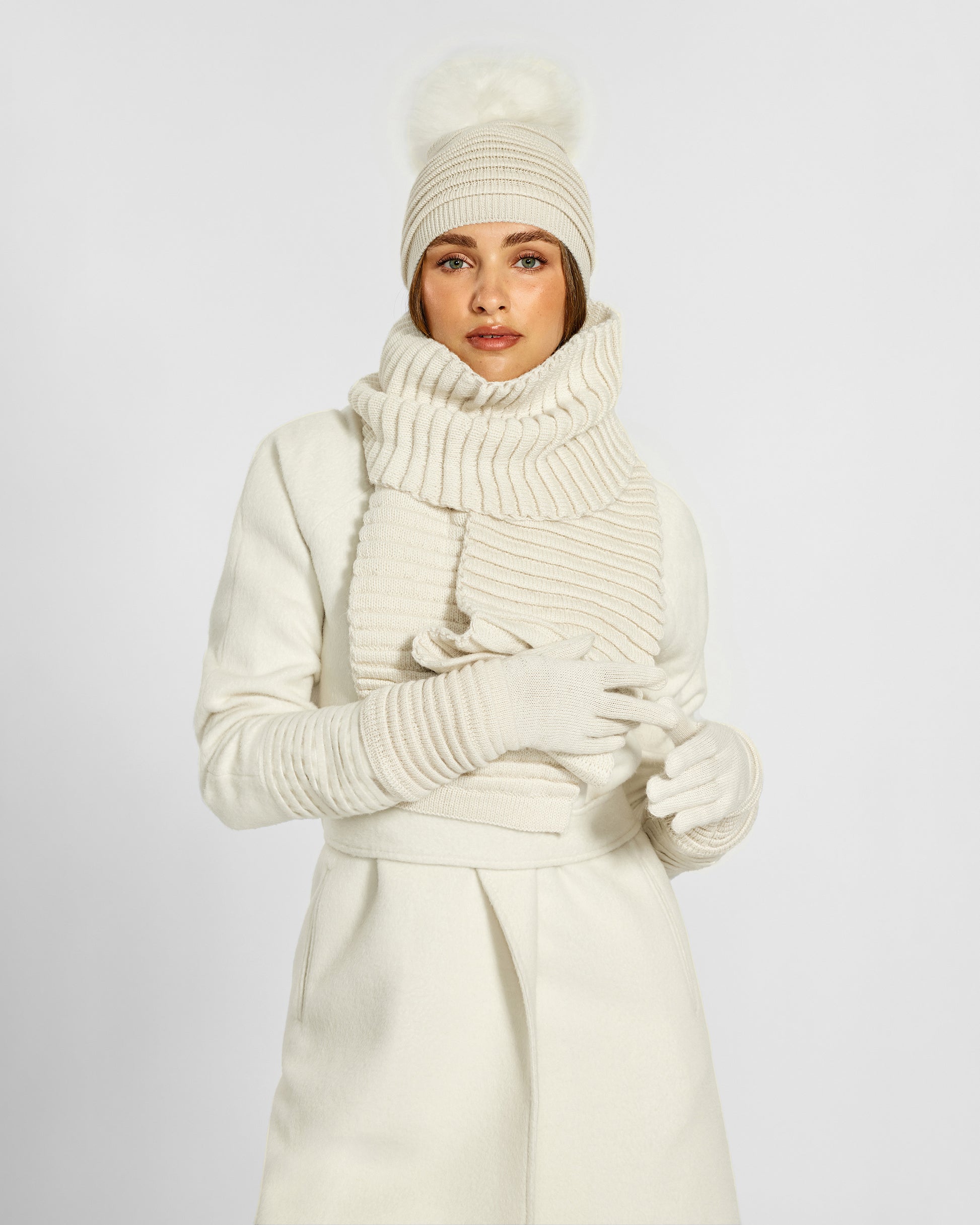 Front view of model wearing Sentaler's adult ivory ribbed gloves, made of baby alpaca yarn, paired with an ivory coat.