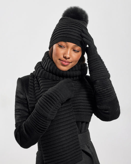 Front close up view of model wearing Sentaler's adult black ribbed gloves, made of baby alpaca yarn, paired with a black coat.