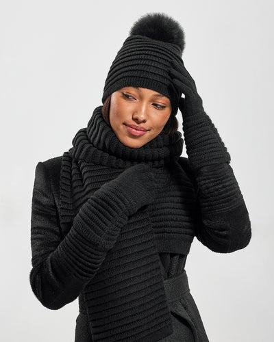 Sentaler Adult Ribbed Black Gloves, Adult Ribbed Black Hat With Fur Pompon, and Adult Ribbed Black Scarf in Baby Alpaca yarn. Seen from front close up on female model.