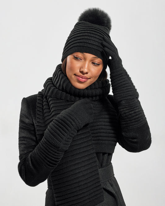 Sentaler Adult Ribbed Black Gloves, Adult Ribbed Black Hat With Fur Pompon, and Adult Ribbed Black Scarf in Baby Alpaca yarn. Seen from front close up on female model.