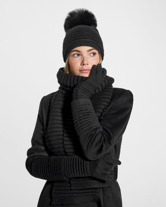Front close up view of model wearing Sentaler's adult black ribbed gloves, made of baby alpaca yarn, paired with a black coat.