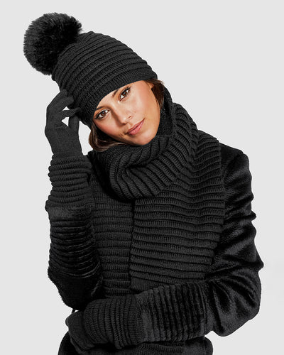   Sentaler Adult Ribbed Black Scarf, Adult Ribbed Black Hat With Fur Pompon, and Adult Ribbed Black Gloves in Baby Alpaca yarn. Seen from front close up on female model.