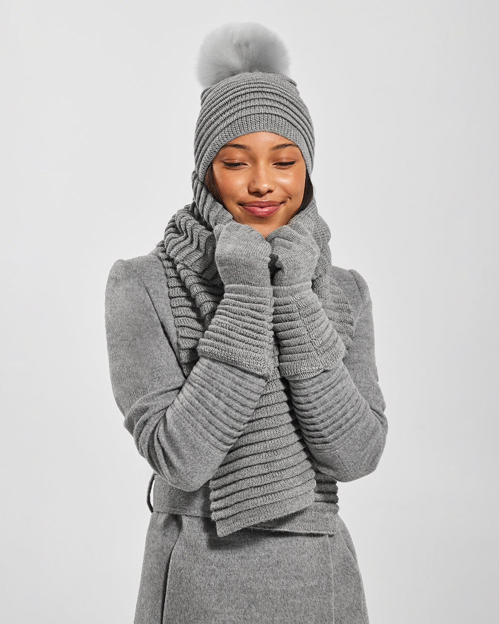 Sentaler Adult Ribbed Grey Hat With Fur Pompon, Adult Ribbed Grey Scarf, and Adult Ribbed Grey Gloves in Baby Alpaca yarn. Seen from front close up on female model.