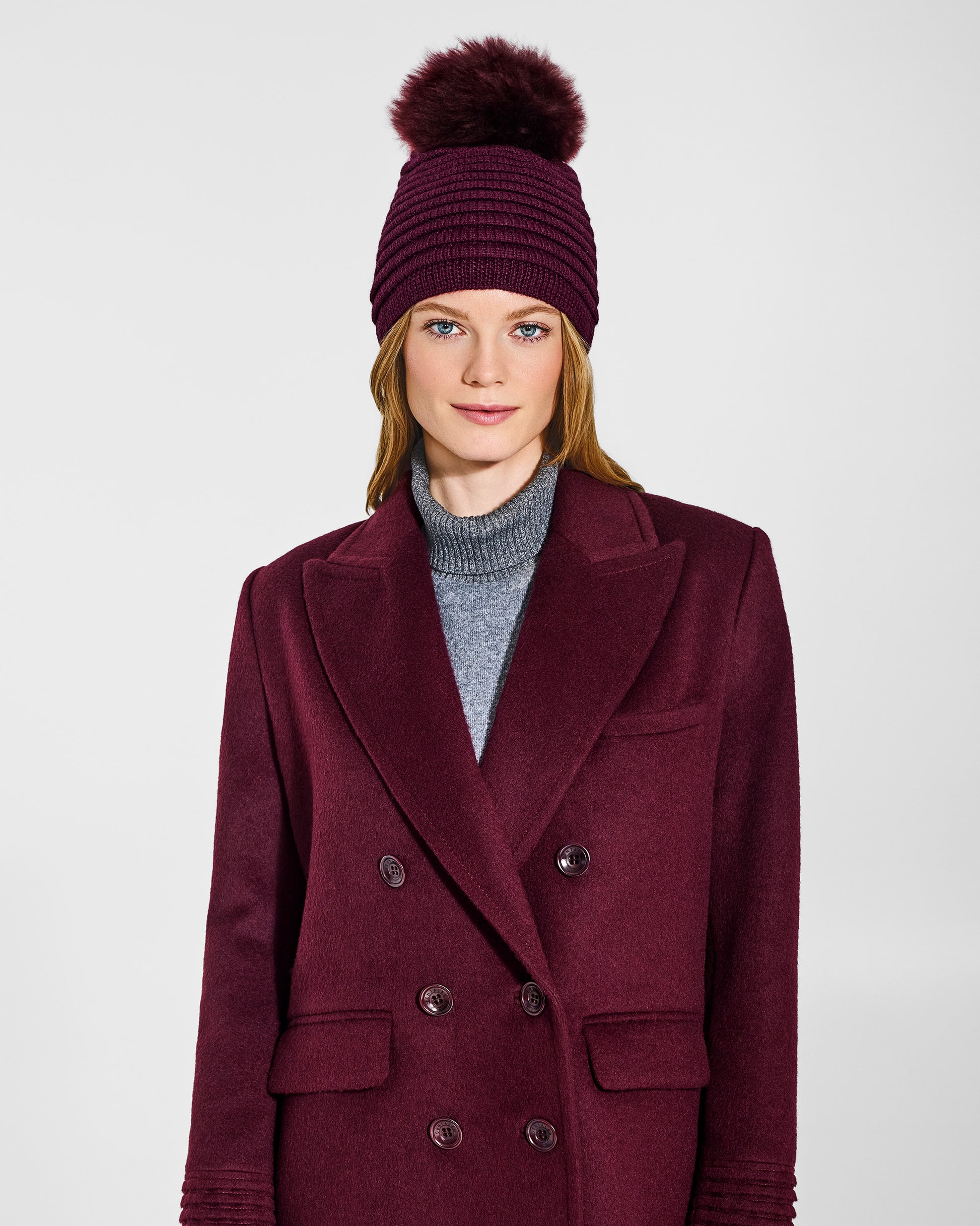 Front view of model wearing Sentaler's adult cherry lacquer ribbed hat with fur pompon, made of baby alpaca yarn paired with a cherry lacquer coat.
