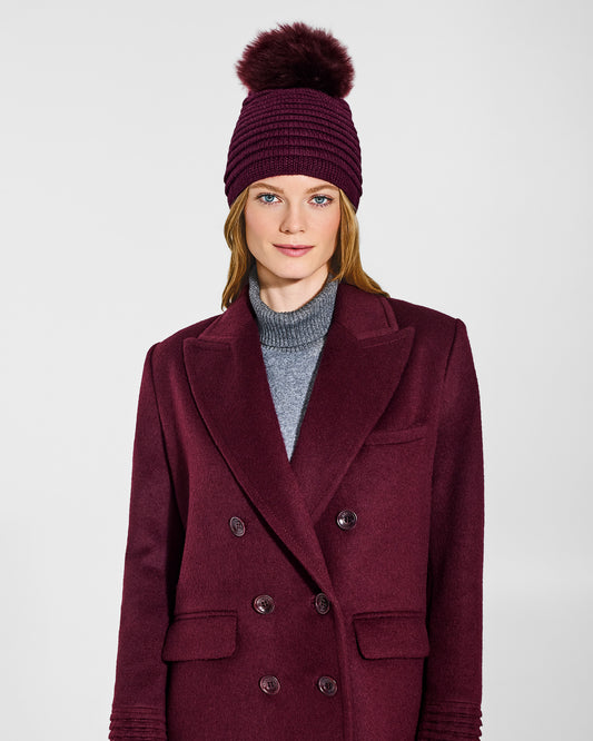 Front view of model wearing Sentaler's adult cherry lacquer ribbed hat with fur pompon, made of baby alpaca yarn paired with a cherry lacquer coat.