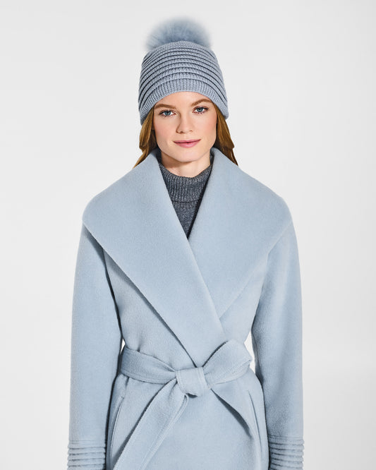 Front view of model wearing Sentaler's adult glacial blue ribbed hat with fur pompon, made of baby alpaca yarn paired with a glacial blue coat.