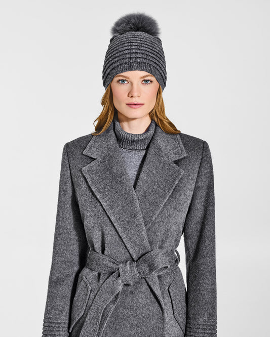 Front view of model wearing Sentaler's adult grey mélange ribbed hat with fur pompon, made of baby alpaca yarn, paired with a grey mélange coat.