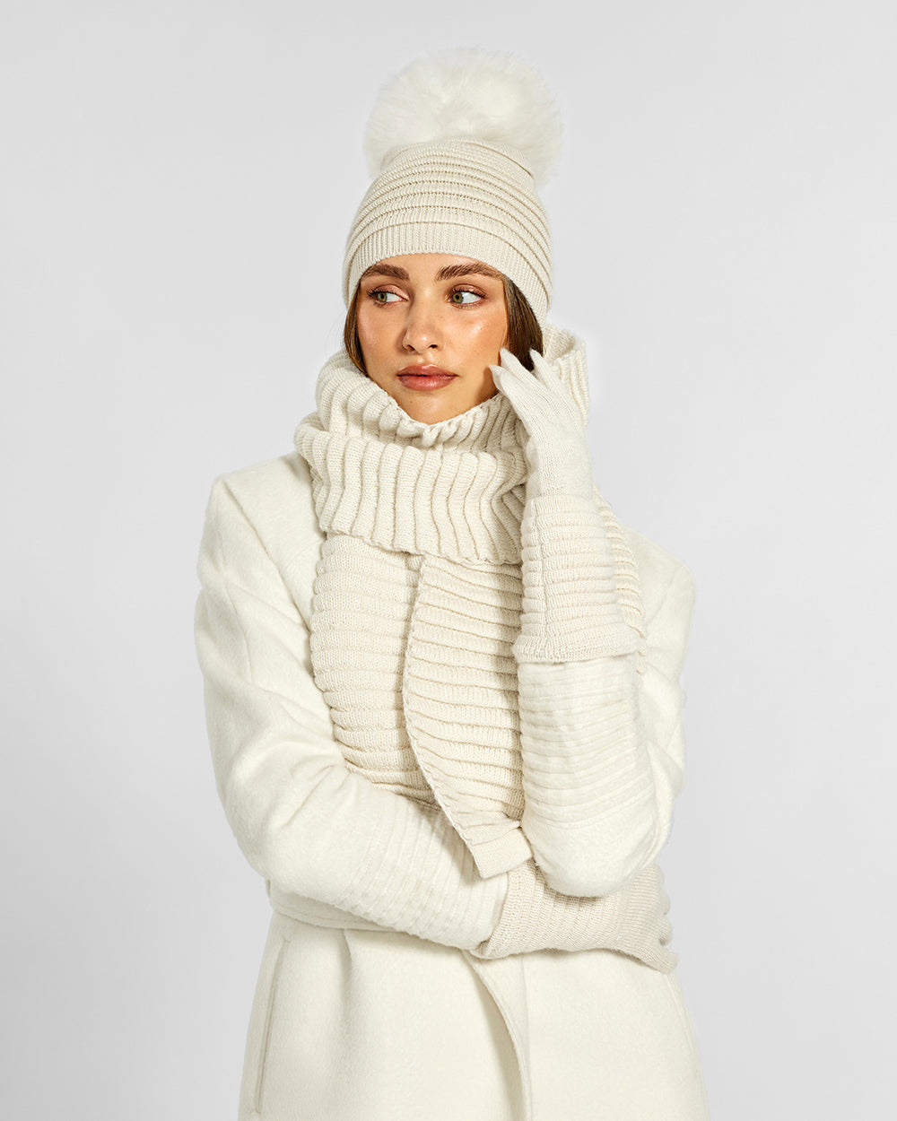 Sentaler Adult Ribbed Ivory Hat With Fur Pompon, Adult Ribbed Ivory Scarf, and Adult Ribbed Ivory Gloves in Baby Alpaca yarn. Seen from front close up on female model.