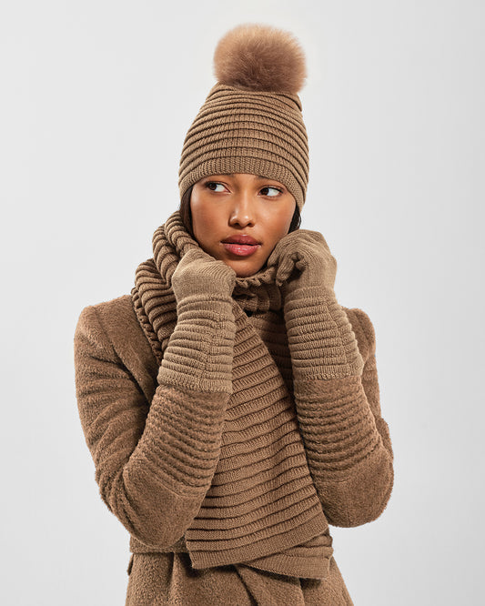 Sentaler Adult Ribbed Dark Camel Hat With Fur Pompon, Adult Ribbed Dark Camel Scarf, and Adult Ribbed Dark Camel Gloves in Baby Alpaca yarn. Seen from front close up on female model.