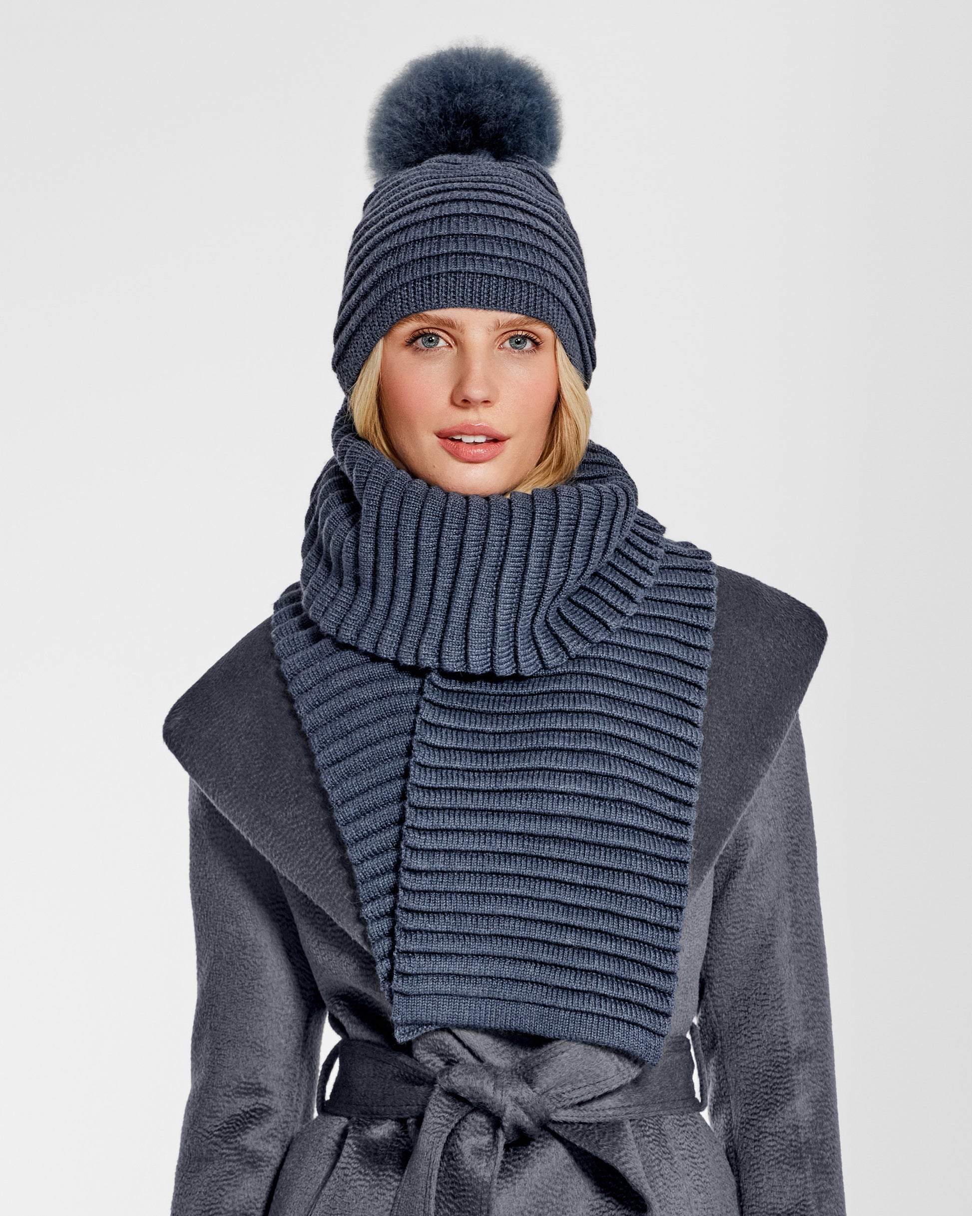 Front view of model wearing Sentaler's adult graphite ribbed hat with fur pompon, made of baby alpaca yarn, paired with a graphite coat.