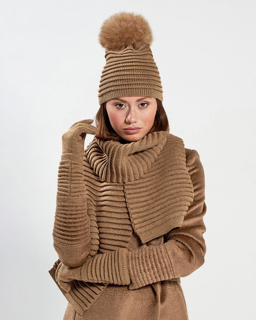 Sentaler Adult Ribbed Dark Camel Scarf, Adult Ribbed Dark Camel Hat With Fur Pompon, and Adult Ribbed Dark Camel Gloves in Baby Alpaca yarn. Seen from front close up on female model.