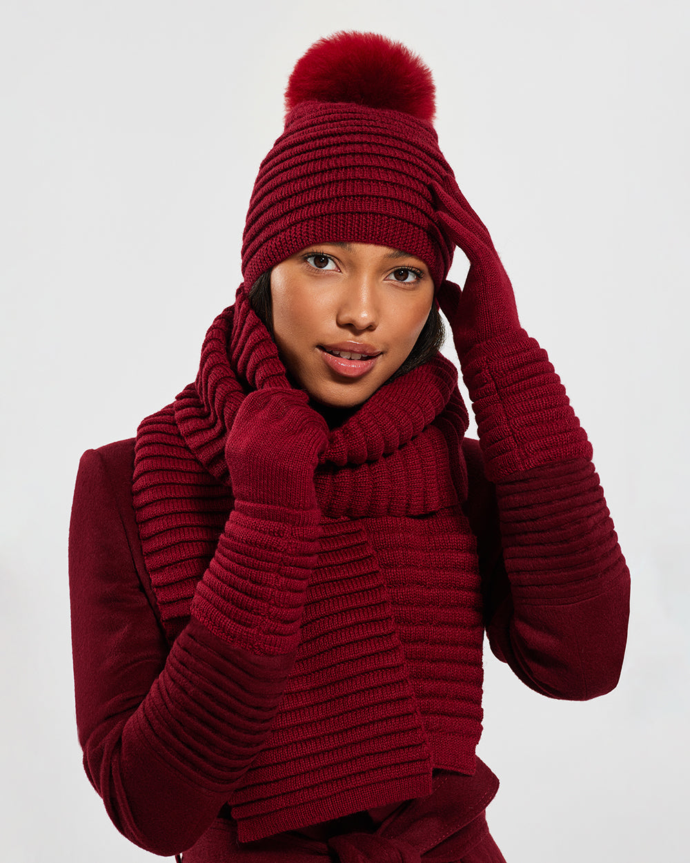 Sentaler Adult Ribbed Garnet Red Scarf, Adult Ribbed Garnet Red Hat With Fur Pompon, and Adult Ribbed Garnet Red Gloves in Baby Alpaca yarn. Seen from front close up on female model.