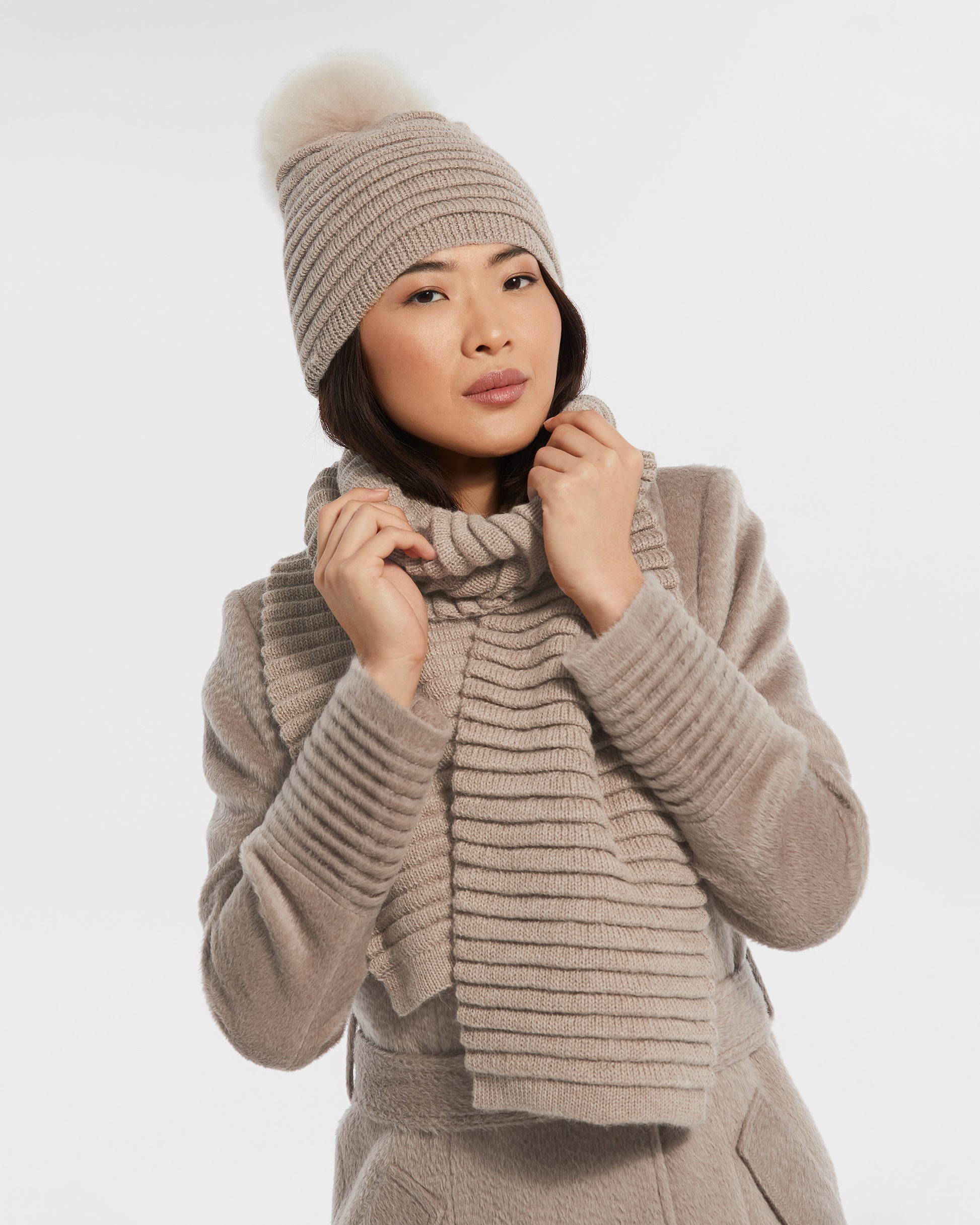 Front view of model wearing Sentaler's adult light taupe ribbed scarf, made of baby alpaca yarn, paired with a light taupe coat.