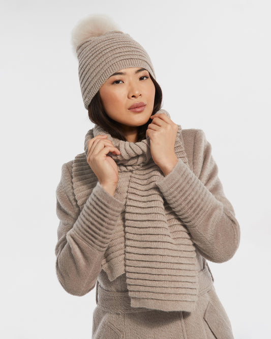 Front view of model wearing Sentaler's adult light taupe ribbed scarf, made of baby alpaca yarn, paired with a light taupe coat.
