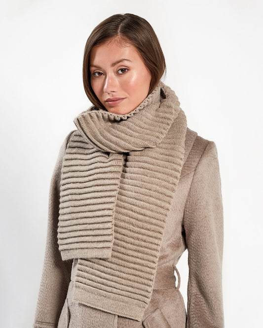 Front view of model wearing Sentaler's adult light taupe ribbed scarf, made of baby alpaca yarn, paired with a light taupe coat.