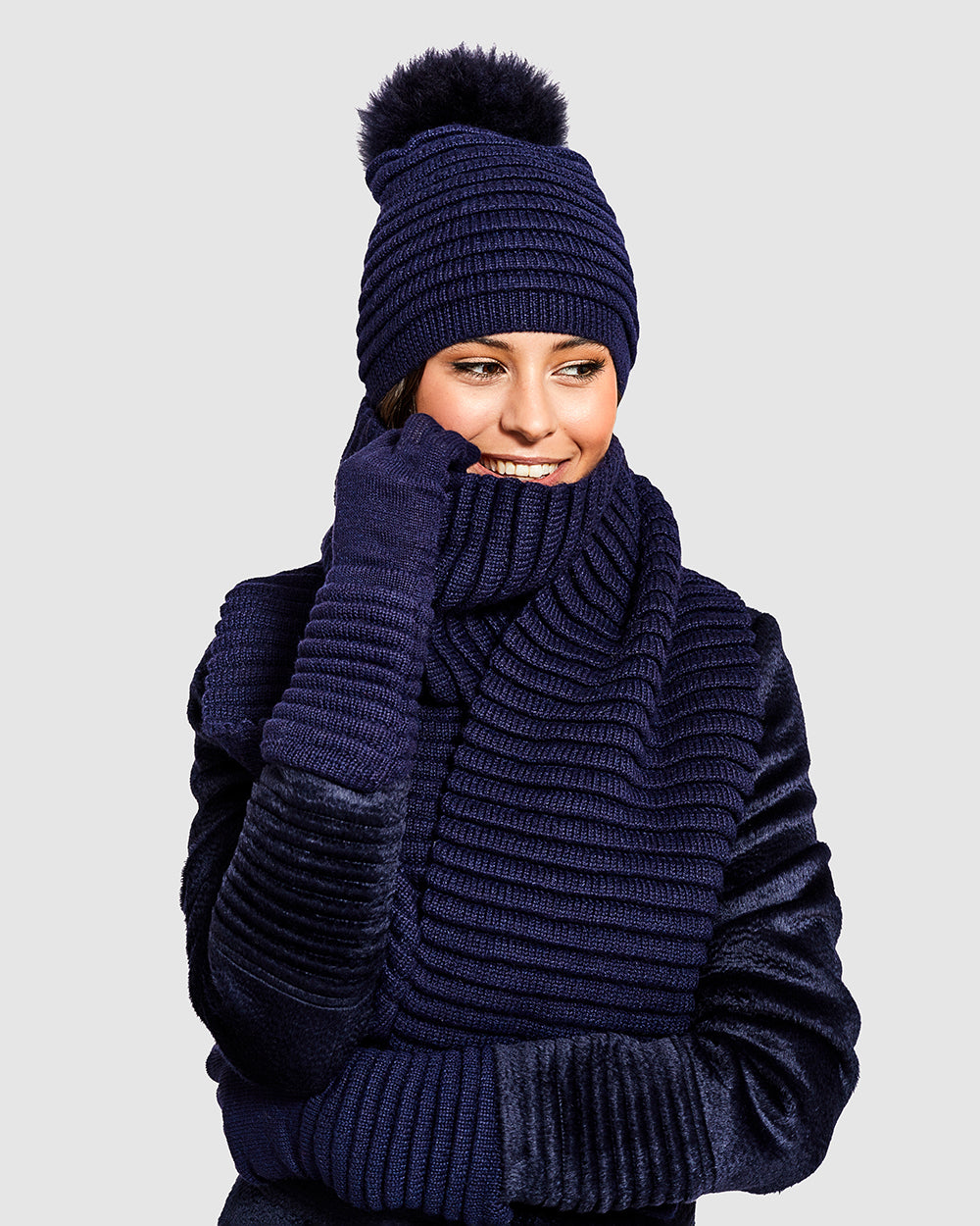 Sentaler Adult Ribbed Navy Scarf, Adult Ribbed Navy Hat With Fur Pompon, and Adult Ribbed Navy Gloves in Baby Alpaca yarn. Seen from front close up on female model.