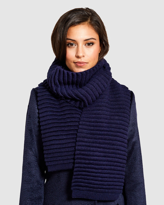 Front view of model wearing Sentaler's adult navy ribbed scarf, made of baby alpaca yarn, paired with a deep navy coat.
