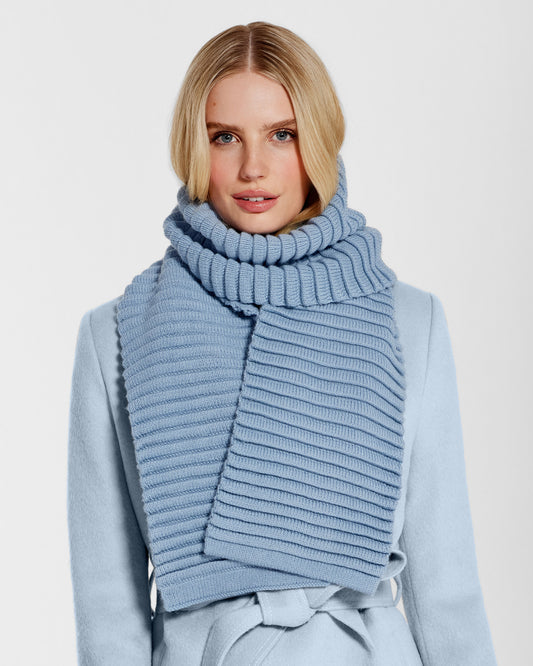 Front view of model wearing Sentaler's adult powder blue ribbed scarf, made of baby alpaca yarn, paired with a powder blue coat.