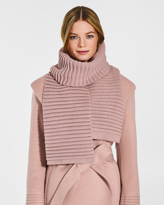 Front view of model wearing Sentaler's adult blush pink ribbed scarf, made of baby alpaca yarn, paired with a blush pink coat.