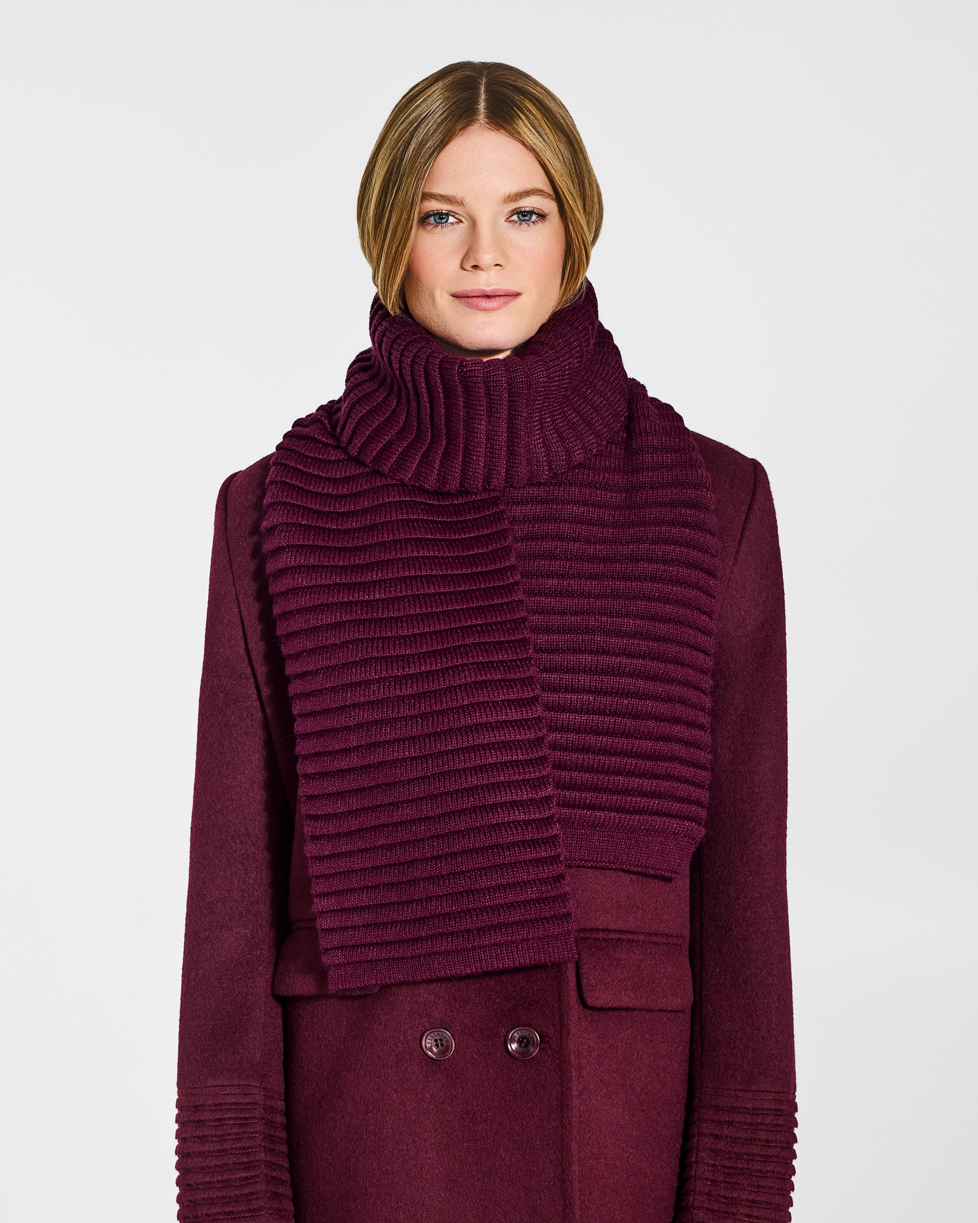 Front view of model wearing Sentaler's adult cherry lacquer ribbed scarf, made of baby alpaca yarn, paired with a cherry lacquer coat.