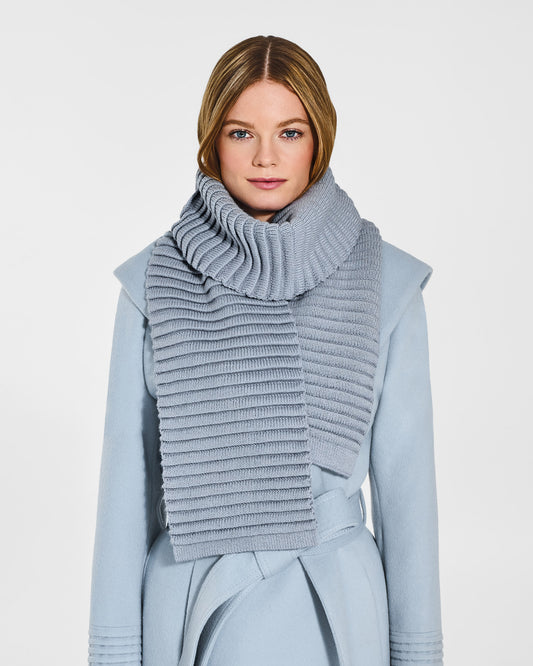 Front view of model wearing Sentaler's adult glacial blue ribbed scarf, made of baby alpaca yarn, paired with a glacial blue coat.