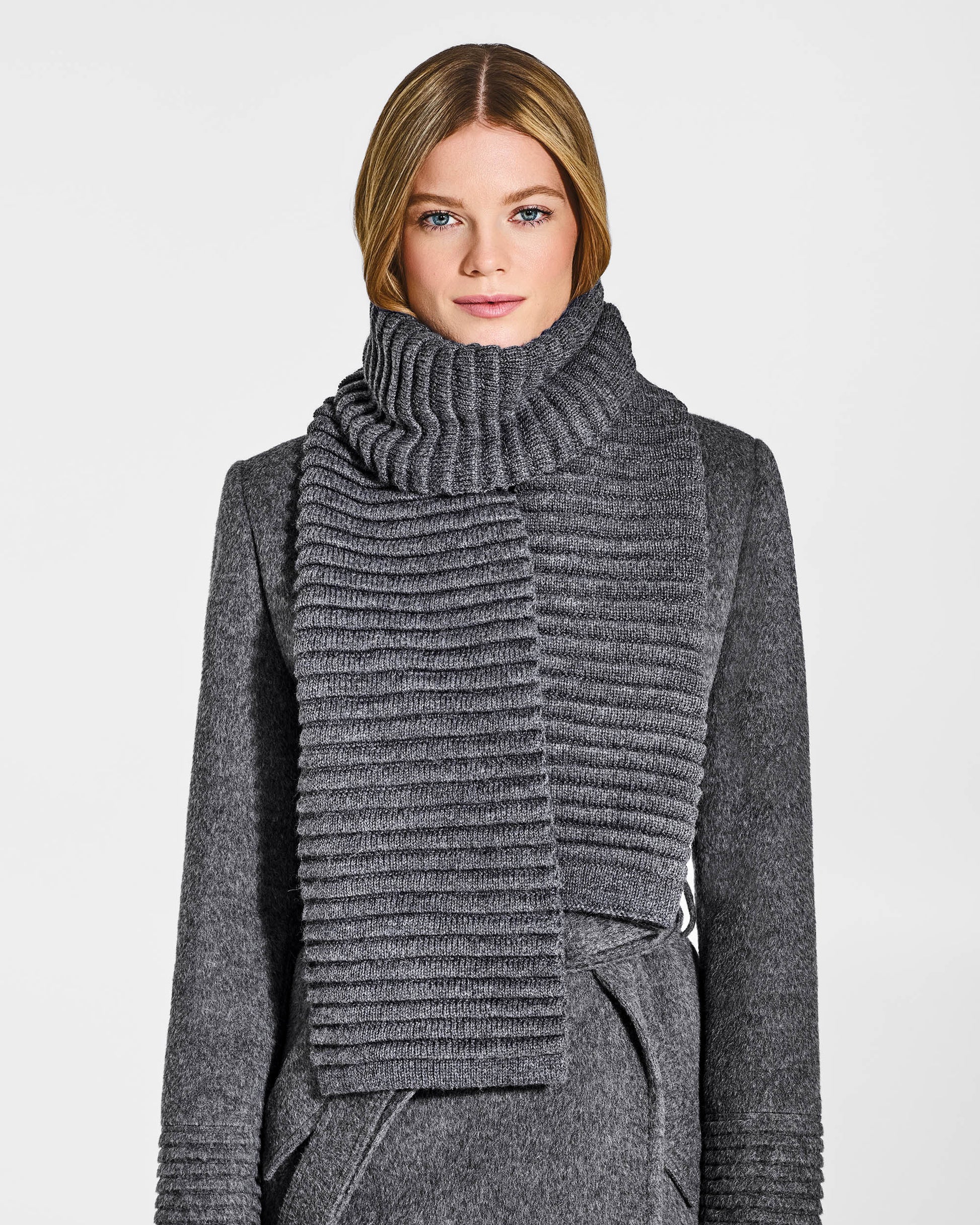Front view of model wearing Sentaler's adult grey mélange ribbed scarf, made of baby alpaca yarn, paired with a grey mélange coat.