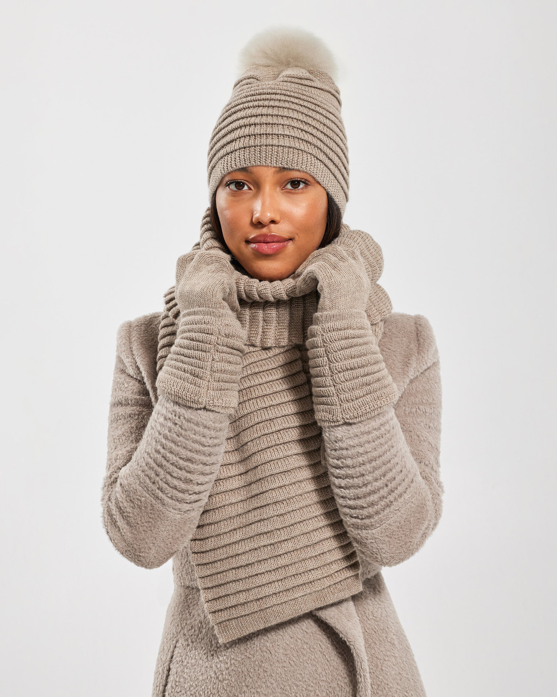 Front view of model wearing Sentaler's adult light taupe ribbed hat with fur pompon, made of baby alpaca yarn, paired with a light taupe coat.