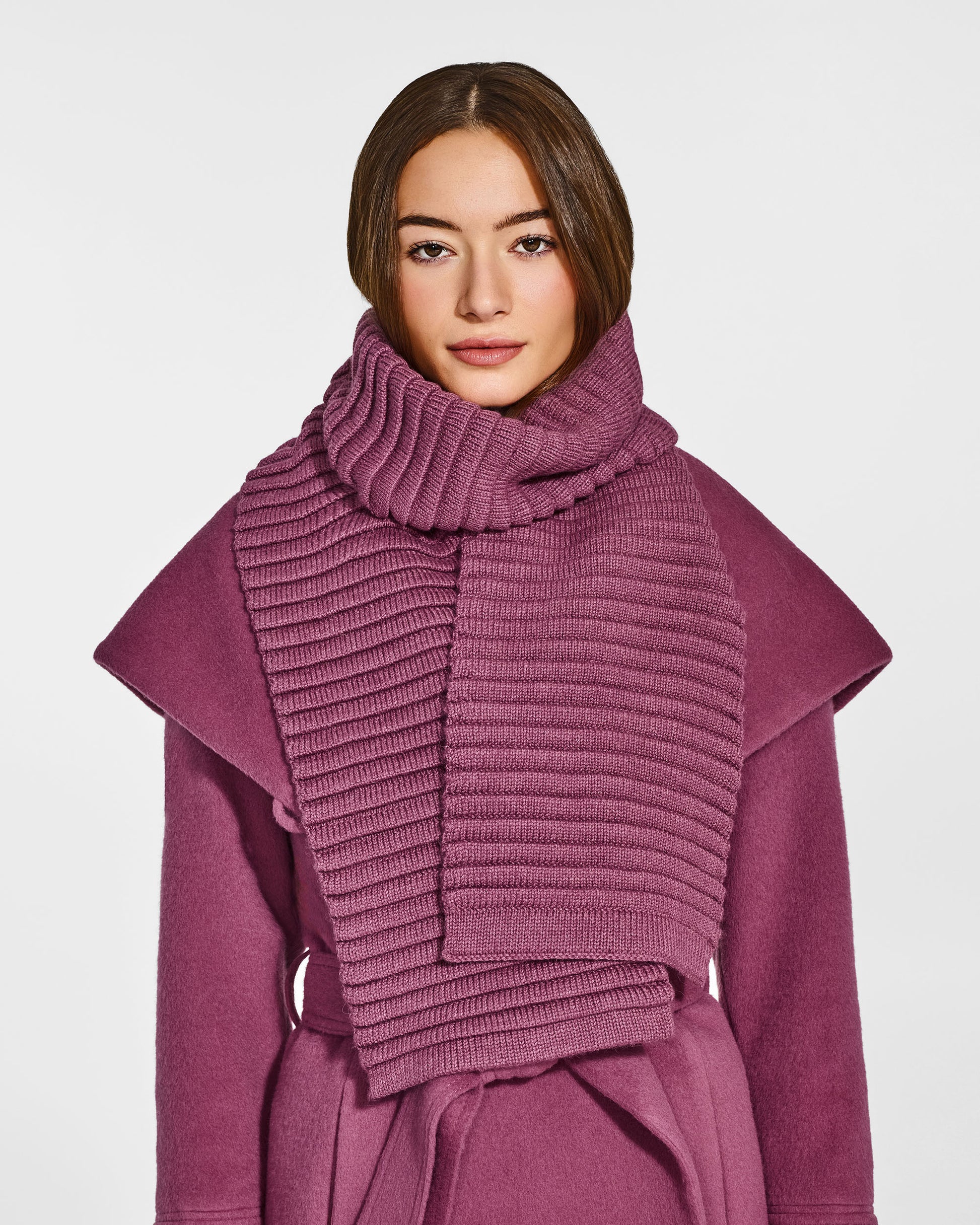 Front view of model wearing Sentaler's adult mauve pink ribbed scarf, made of baby alpaca yarn, paired with a mauve pink coat.