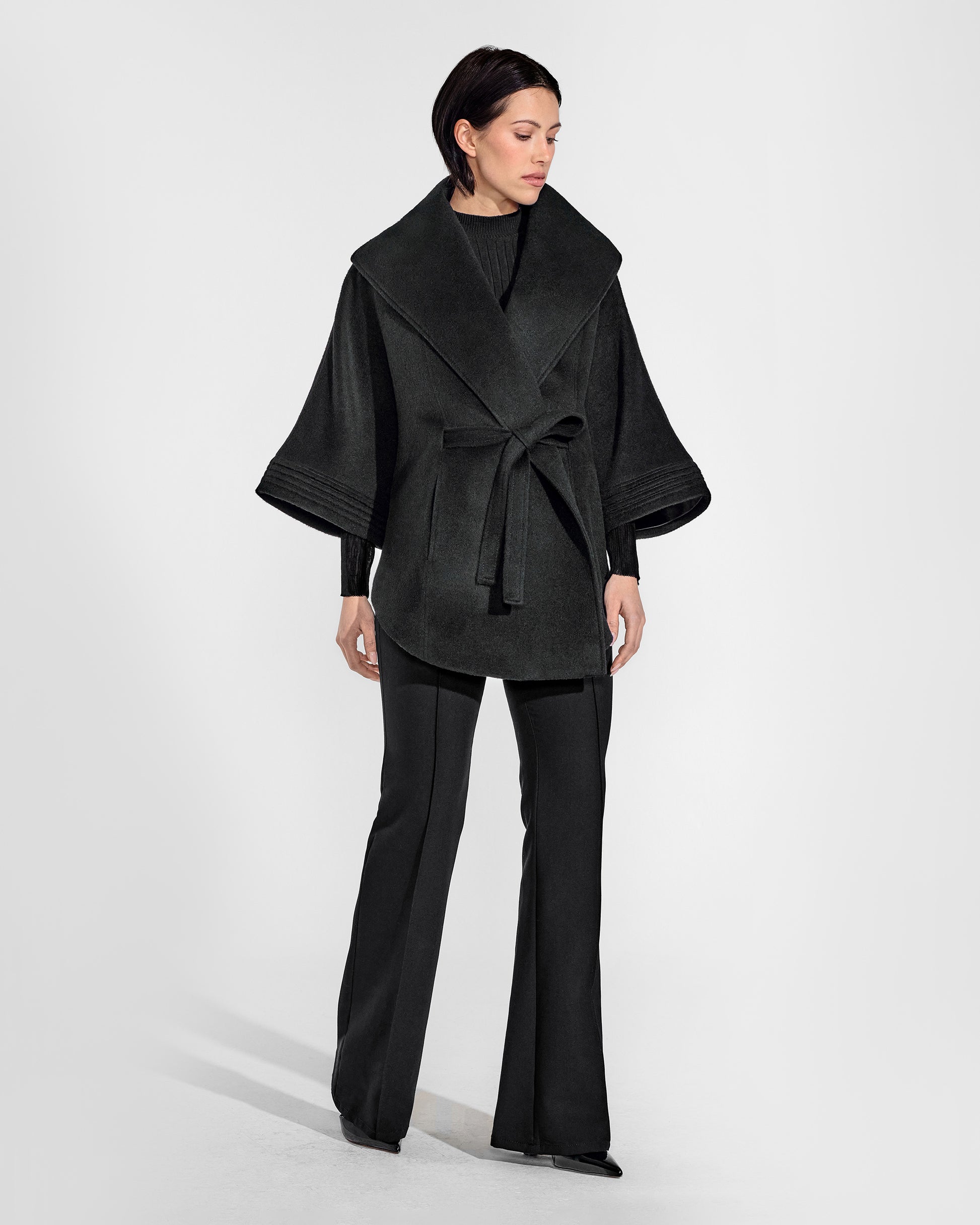 Front view of model wearing a Sentaler black cape made of baby alpaca wool, with a shawl collar, worn belted.