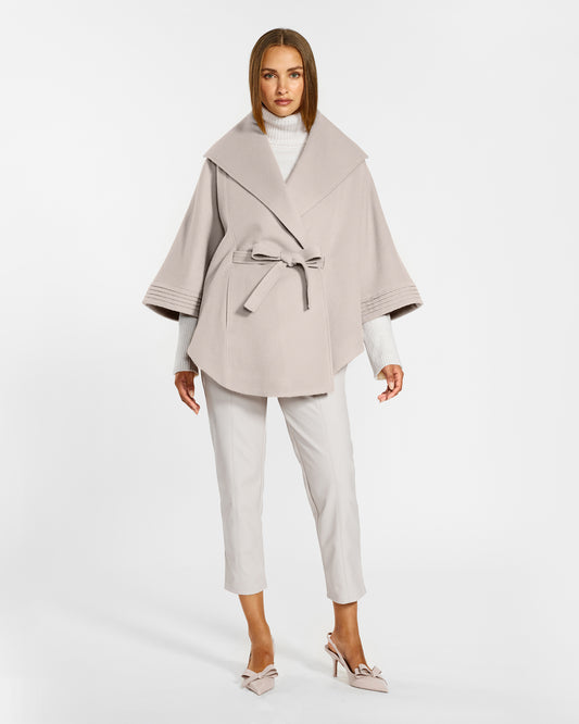 Front view of model wearing a Sentaler bleeker beige cape made of baby alpaca wool, with a shawl collar, worn belted.