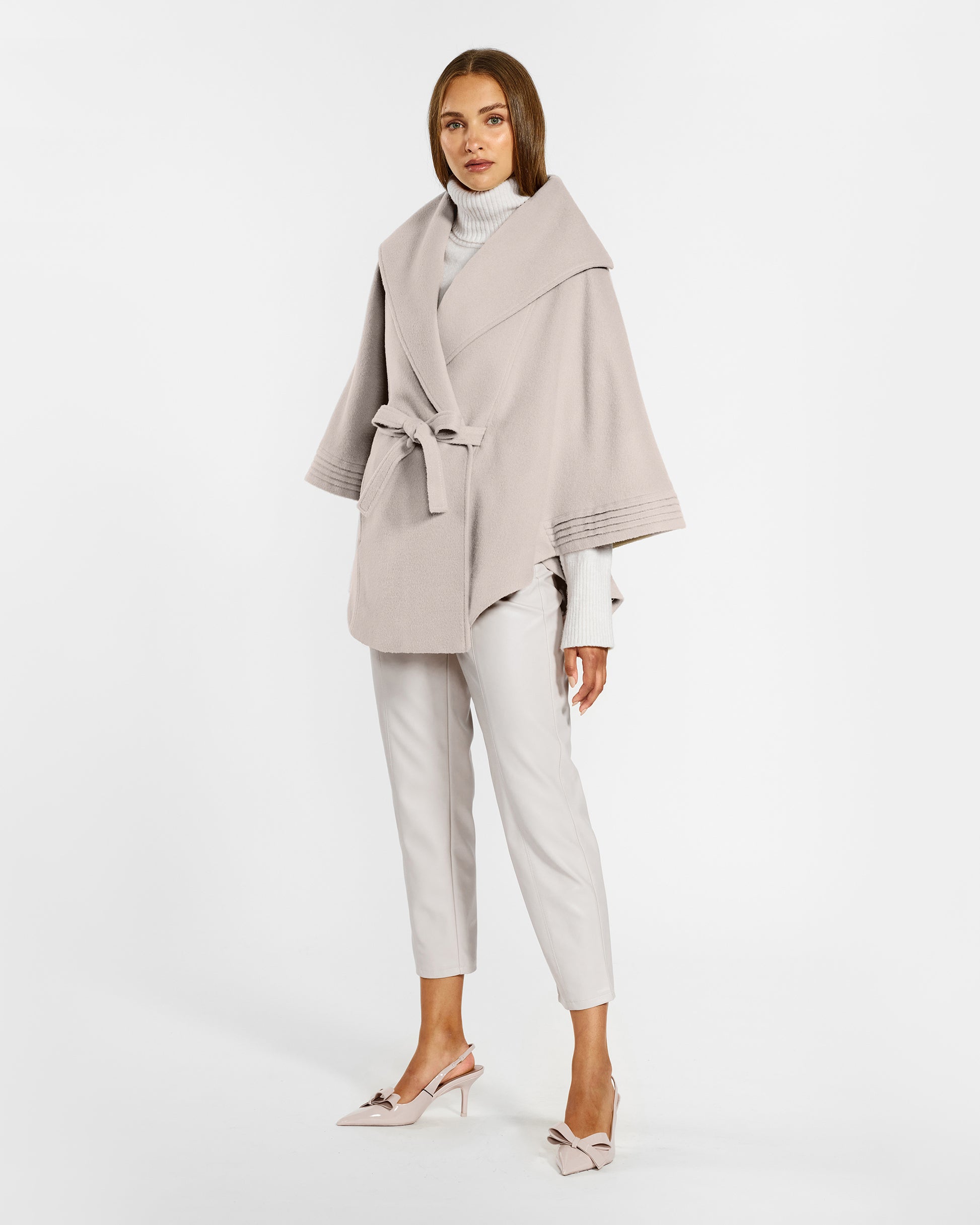 Side view of model wearing a Sentaler bleeker beige cape made of baby alpaca wool, with a shawl collar, worn belted.