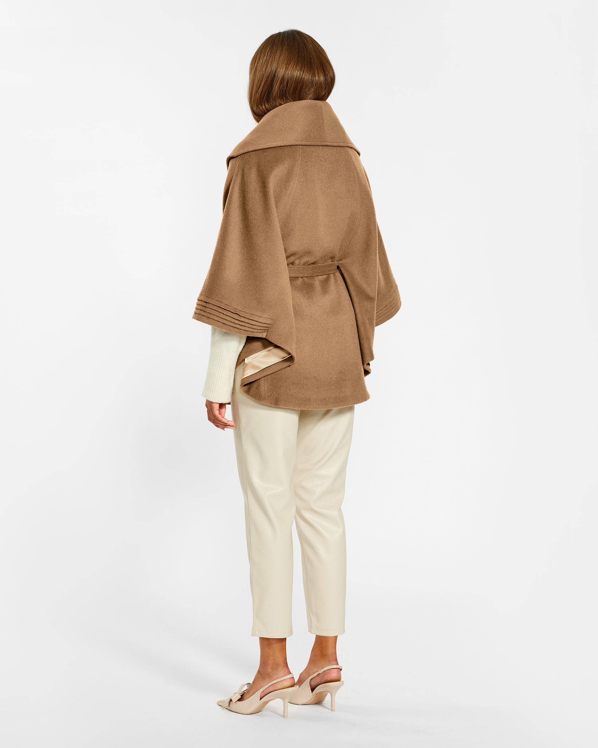 Back view of model wearing a Sentaler dark camel cape made of baby alpaca wool, with a shawl collar, worn belted.