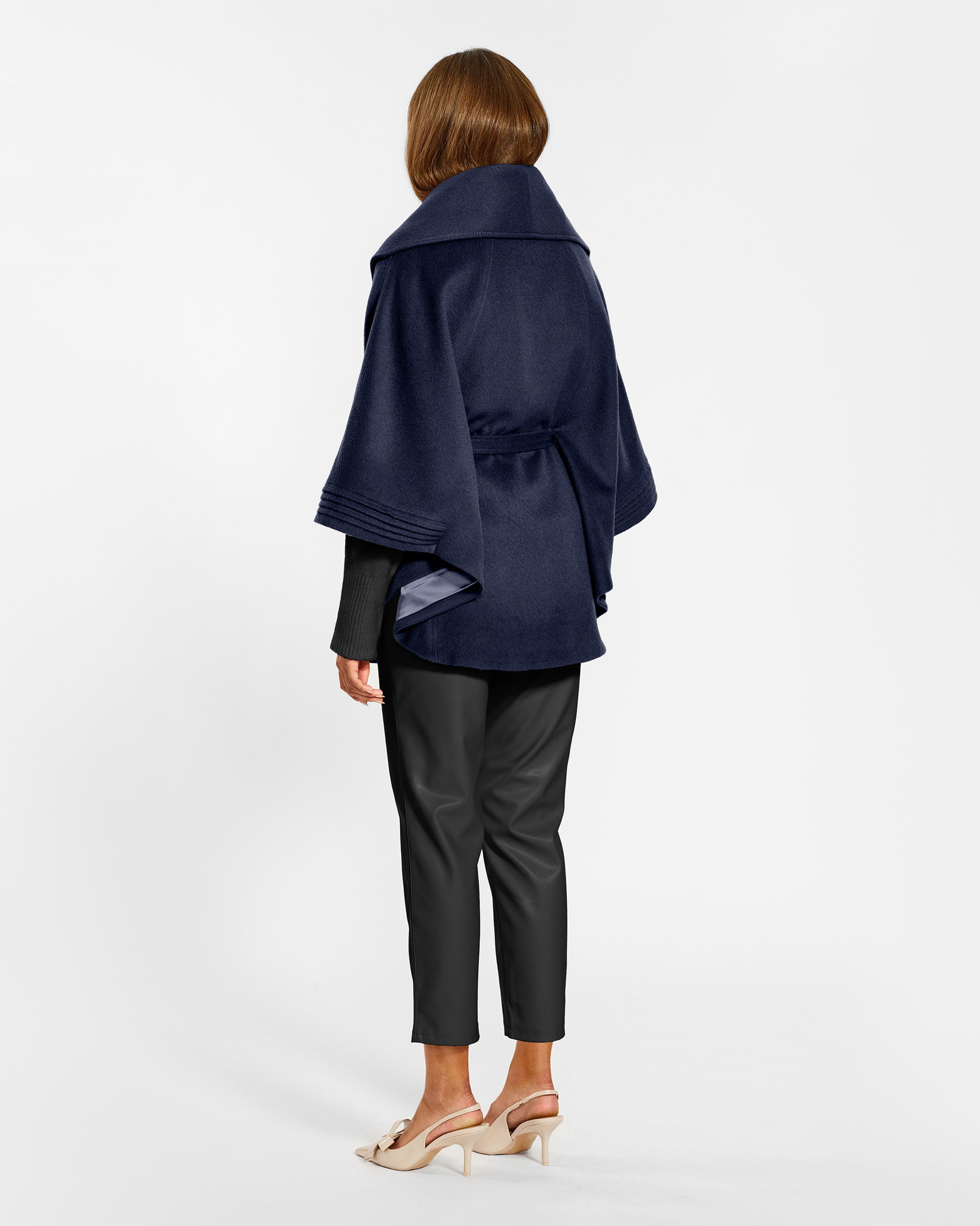 Back view of model wearing a Sentaler deep navy cape made of baby alpaca wool, with a shawl collar, worn belted.
