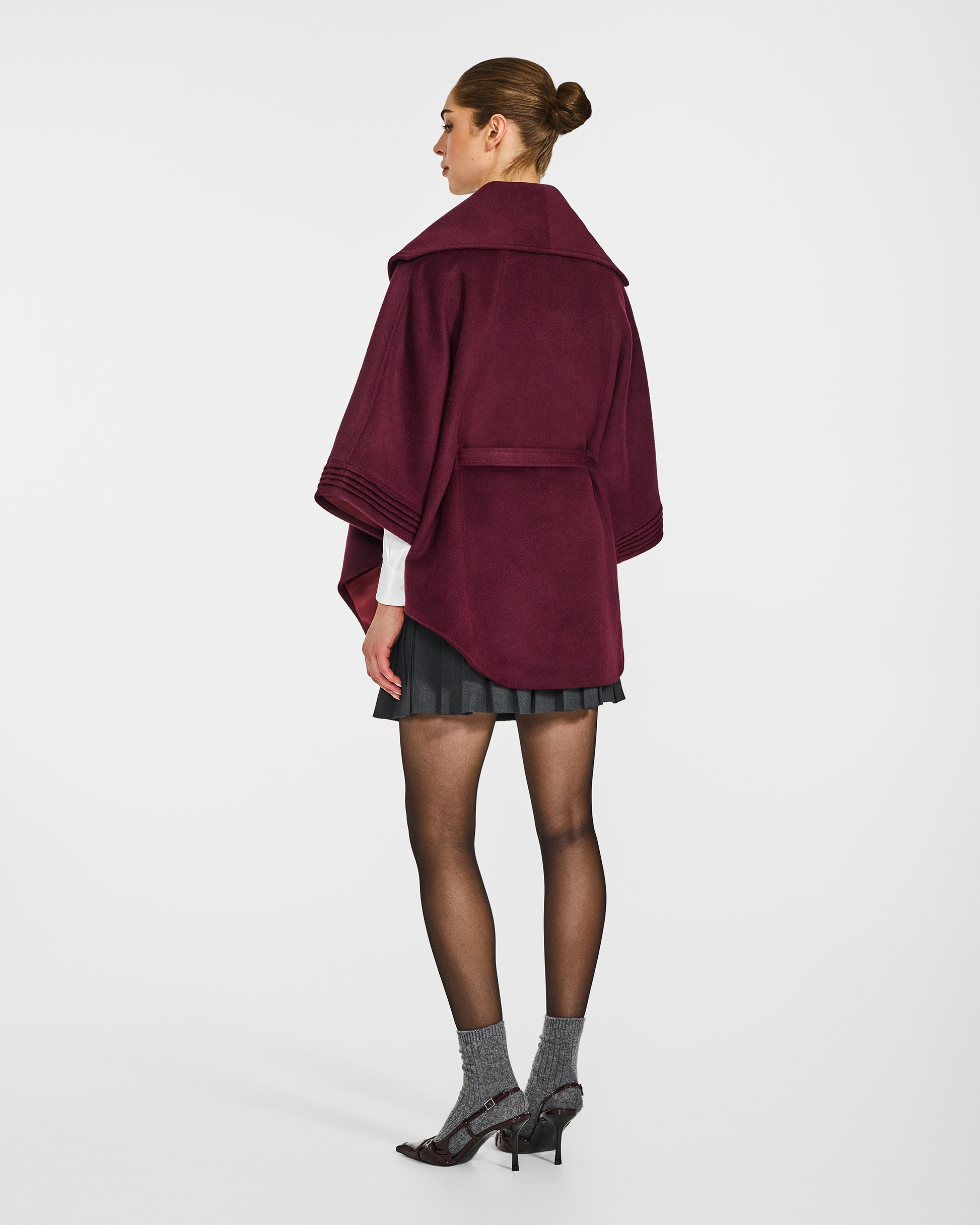 Back view of model wearing a Sentaler cherry lacquer cape made of baby alpaca wool, with a shawl collar, worn belted.